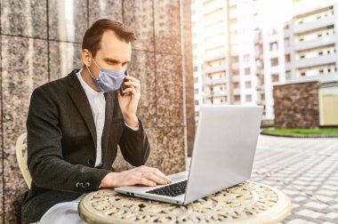 Koruyucu maskeli adam dizüstü bilgisayarla çalışıyor.