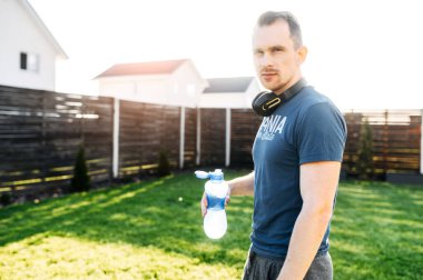 Adam elinde bir şişe suyla dışarıda duruyor.