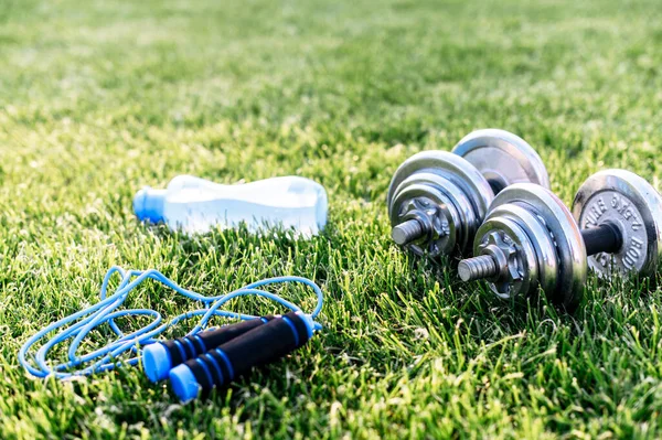 Гантели, бутылка воды и скакалка на траве — стоковое фото