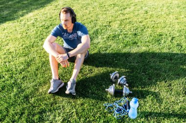 Spor kıyafetli bir adam çimenlerde oturuyor.