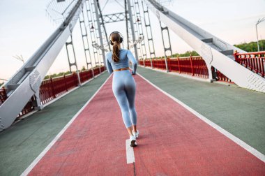 Genç kadın şehir köprüsünde koşuyor.