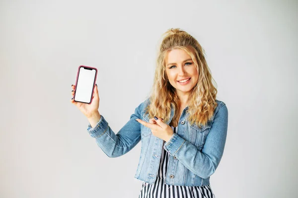 Mujer joven señala con el dedo a una pantalla de teléfono en blanco — Foto de Stock