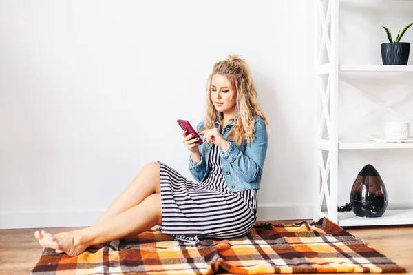 Blondes Mädchen zu Hause mit einem Handy in der Hand — Stockfoto