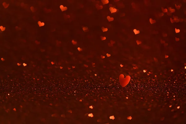 Red small heart on glittering background with hearts shaped bokeh.