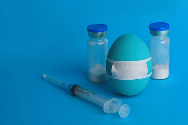 One blue Easter egg in protective mask with medicine thing around.