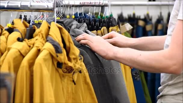 Un hombre que elige la chaqueta del tamaño correcto de un estante — Vídeo de stock