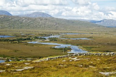 Dağlar, dolambaçlı su ve taştan bir duvar ile bir manzara.