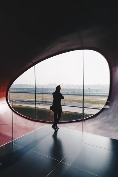 Mujer de pie en un edificio de oficinas futurista y moderno, mirando hacia el exterior - ventana moderna ovalada  . — Foto de Stock