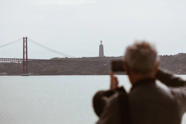Lizbon - Portekiz köprüsünde akıllı telefon ile bulanık kıdemli adam alarak resim — Stok fotoğraf