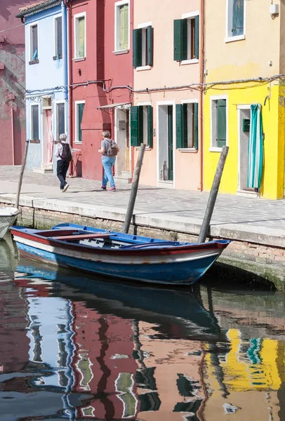 Two Senior woman walking along waterways with traditional colorful facade of Burano and reflection. Venice — Stock Photo, Image