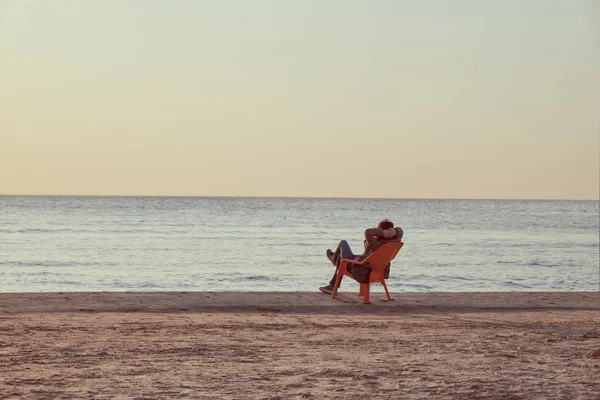 Женщина или девушка сидят в кресле и смотрят на море и отдыхают на пляже зимой на закате . — стоковое фото