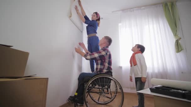 Amado marido pessoa com deficiência em cadeira de rodas com sua família amigável, escolhe novo papel de parede para sala de reparação — Vídeo de Stock
