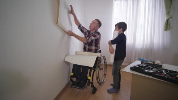 Repair in apartment, caring father disabled person in wheelchair with beloved son choose wallpaper in room, relationship of parents and children — Stock Video