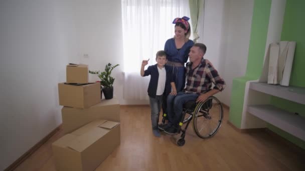Молодая семья с отцом-инвалидом в инвалидной коляске счастливо переезжает и обсуждает меблировку в новой квартире — стоковое видео