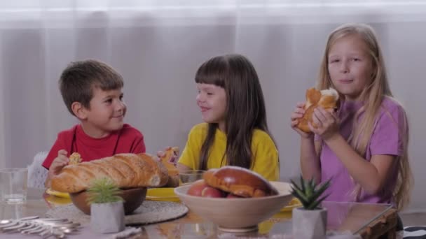 Niñez despreocupada, niño feliz y chicas sonrientes sentadas en la mesa dulce comiendo pasteles aromáticos después de la fiesta festiva de los niños — Vídeos de Stock