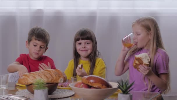 Kinderen eten, vrolijk gezelschap van vrienden van kinderen neemt een middagsnack, bijt gebak en drinkt sap op kinderfeestje — Stockvideo