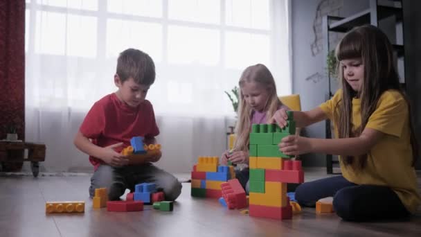 Lustige Kinder spielen leidenschaftlich gerne Konstrukteursspiele und sammeln Spielzeug aus farbigen Teilen und Blöcken für die Geschwindigkeit, wer ist schneller — Stockvideo