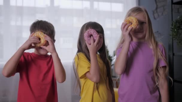 Feliz infancia, los niños despreocupados miran con un ojo a través de la rosquilla durante la celebración conjunta, fiesta de los niños — Vídeos de Stock