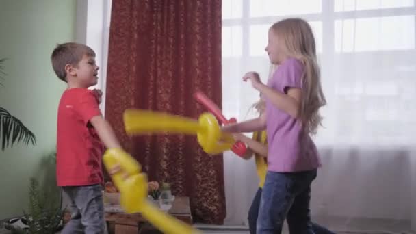 Улыбающиеся друзья девушки активно борются с мальчиком на воздушных шарах во время празднования детской вечеринки — стоковое видео