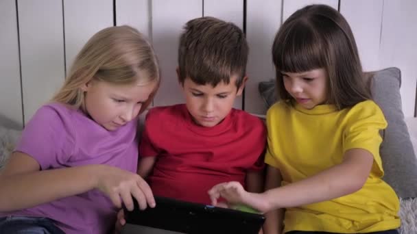 Bambini moderni, bambino con le ragazze scivolare il dito sul touch screen del computer tablet durante il relax su un letto a casa — Video Stock