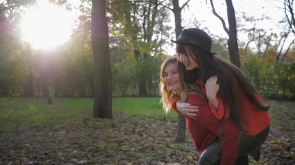 Sonrientes hermosas novias divertirse y hacer piggyback de vacaciones en otoño parque en temporada de otoño, concepto de amistad — Vídeo de stock