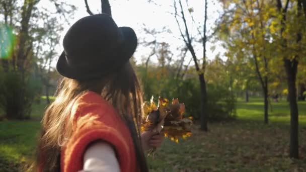 Chica atractiva en el parque de otoño, mujer divertida joven en sombrero corre alegremente y toma de la mano de un amigo durante el fin de semana conjunto en la temporada de otoño — Vídeo de stock
