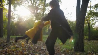 Neşeli kadın ebeveyn, güzel kızıyla dışarıda yürürken sonbahar parkında ellerini bükerek oynuyor.