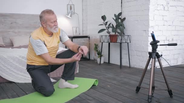 Influenceurs blogueur, vieil homme prend examen de montres intelligentes pour vlog recommander à son public d'abonnés un appareil assis sur tapis de yoga dans la chambre avec l'intérieur moderne — Video