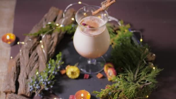 Cocktail di uova tradizionale in bel bicchiere preparato per la festa festiva decorata con un albero di Natale e cannella sullo sfondo di luci — Video Stock