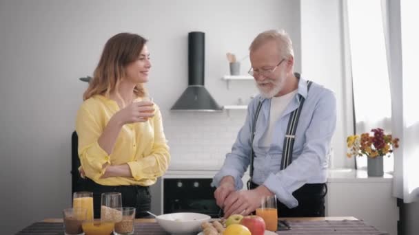 Χαρούμενα κοινωνικότητα εγγονή χαρούμενα συνομιλίες και ποτά χυμό στην κουζίνα με τον αγαπημένο παππού της σε γυαλιά για την όραση, ενώ κάνει πρωινό από υγιεινά προϊόντα, υγειονομική περίθαλψη — Αρχείο Βίντεο