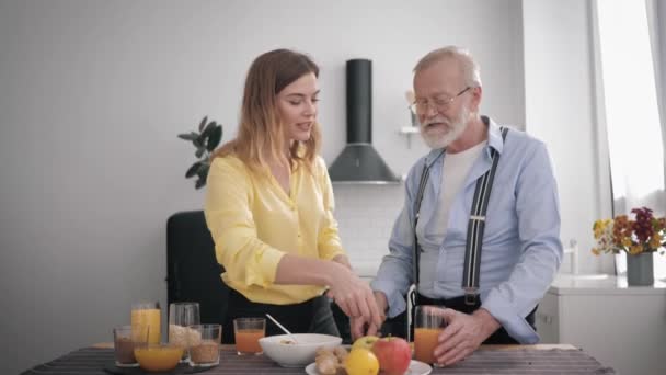 Relacionamentos familiares, sorrindo menina adulta ajuda seu avô velho preparar salada de vitaminas de produtos saudáveis, enquanto se divertindo juntos na cozinha — Vídeo de Stock