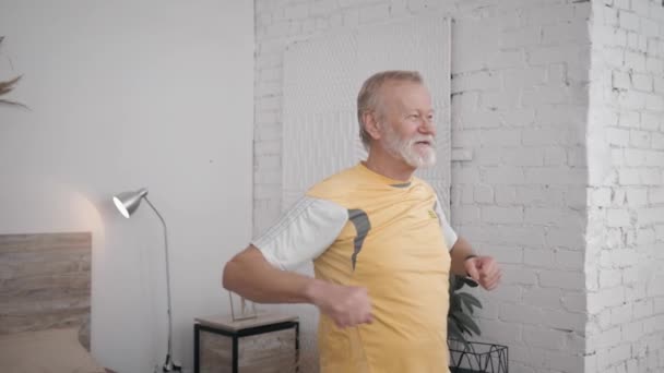 Sonriente abuelo fanático de los deportes y estilo de vida saludable realiza ejercicios útiles para mantener la vitalidad en su habitación con interior creativo — Vídeo de stock