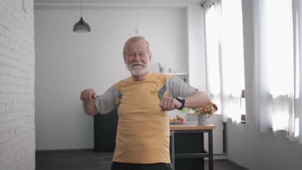 Ejercicios de bienestar, un hombre de edad avanzada se ocupa de la salud realiza ejercicios agitando los brazos mientras está de pie en el interior — Vídeos de Stock