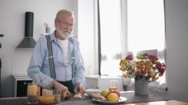 Doğru beslenmeyi seven gözlüklü yaşlı enerjik adam sağlıklı meyve suyu hazırlar. Vitamin suyu içerken güzel bir mutfağın arka planında durur.