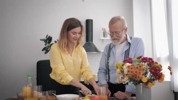 Pflege der älteren Generation, fröhlich lächelnde Enkelin mit ihrem pfeffrigen Opa haben Spaß beim Reden und Zubereiten eines gesunden Frühstücks, um in der Küche am Tisch gesund zu bleiben — Stockvideo