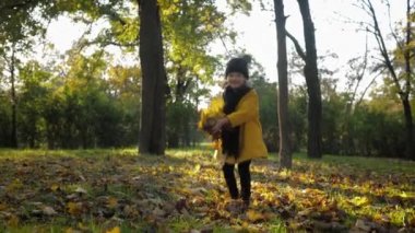 Neşeli çocuk, güzel küçük kızın portresi dışarıda eğleniyor sonbahar parkında sarı yapraklarla oynuyor.