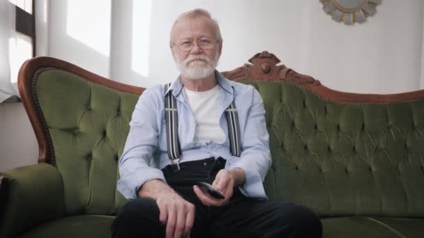 Rodinné vztahy, šťastné generace starý otec s šedivými vlasy a brýle smích objímající mladé dcery dávat sedět na pohovce doma — Stock video