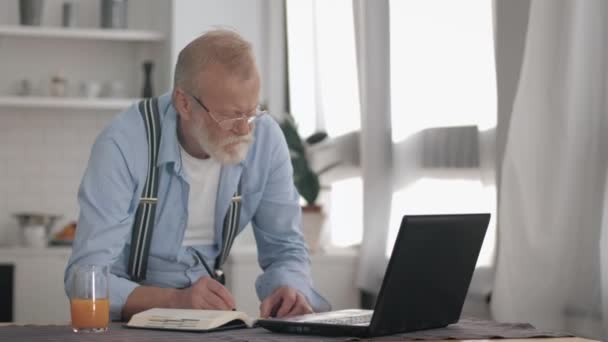 Homem idoso barbudo bonito em óculos trabalhando freelance no computador portátil em casa leva estilo de vida moderno ativo de pessoas mais velhas — Vídeo de Stock