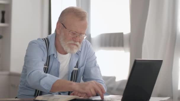 在现代，有魅力的养老金领取者，戴着灰色胡须，戴着眼镜，在网上为电脑支付公用事业费 — 图库视频影像
