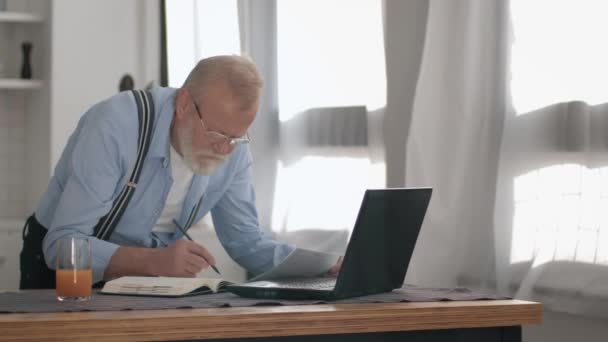 Upset modern pensioner male nervous working at laptop deals with unpaid bills and payments writes in notebook, freelancer — Stok video