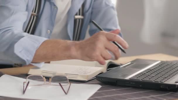 Idoso aposentado conta contas de serviços públicos on-line, escreve dados para um notebook e trabalha em computador portátil sentado à mesa, close-up — Vídeo de Stock