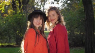 autumn season, funny female friends are laughing and call to play with fyellow leaves in sunshine into warm day at park while holiday outdoor