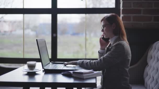 Business online success concept, happy businesswoman enjoys good news received from the employees by phone showing yes sign working remotely at laptop computer making notes in notebook — Stock Video