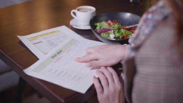 Plan de dieta, oportuna joven hermosa niña supervisa su dieta y cuenta el contenido calórico sentado en la mesa en la cafetería, concepto de alimentación saludable — Vídeos de Stock