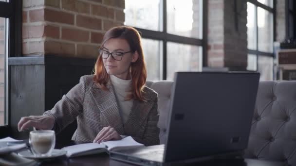 Online business management, moderne zakenvrouw in bril voor visie werkt op afstand op de computer en controleert rapporten op de smartphone tijdens het zitten in cafe, nuttige gadgets — Stockvideo