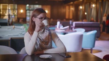 Kahve molası, gözlüklü çekici bir kadın kafede dinlenmeyi, lezzetli kahve içmeyi ve şık bir restoranda masada otururken kameraya bakmayı seviyor.