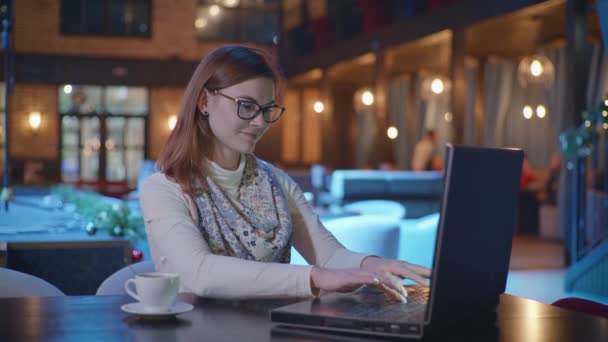 Afstand werk, jonge succesvolle vrouwelijke werknemer in glazen voor het zicht werken op laptop computer en verheugt zich over goede informatie ontvangen terwijl zitten aan tafel in trendy cafe wifi — Stockvideo