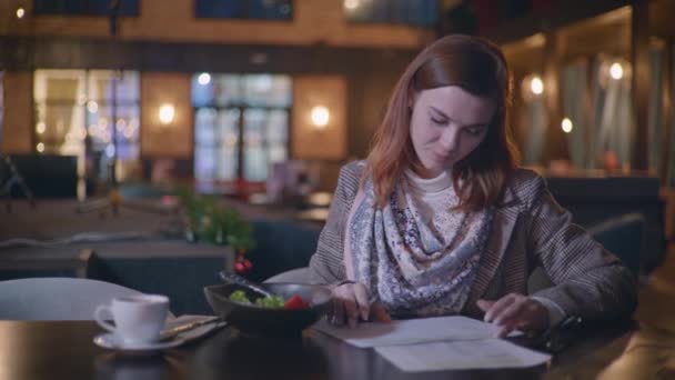 Dieta elegante, uma jovem menina sorrindo cuida do peso conta o número de calorias na salada de legumes frescos notas no plano de dieta enquanto desfruta de jantar em um restaurante caro. — Vídeo de Stock