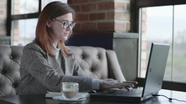 Portret van vrolijk lachend meisje, jonge zakenvrouw werkt op laptop computer, het controleren van online boekhoudkundige rapporten tijdens koffiepauze zitten aan tafel door raam in prestigieuze restaurant — Stockvideo