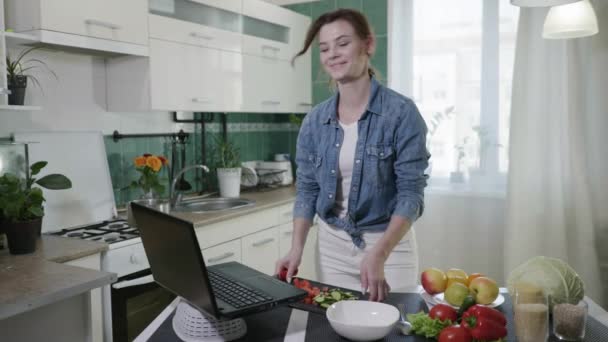 Attraktive Hausfrau auf Diät Zubereitung vegetarischer Salat mit frischem Gemüse nach Videorezept aus dem beliebten Blog über gesunde Ernährung im Stehen am Tisch in — Stockvideo